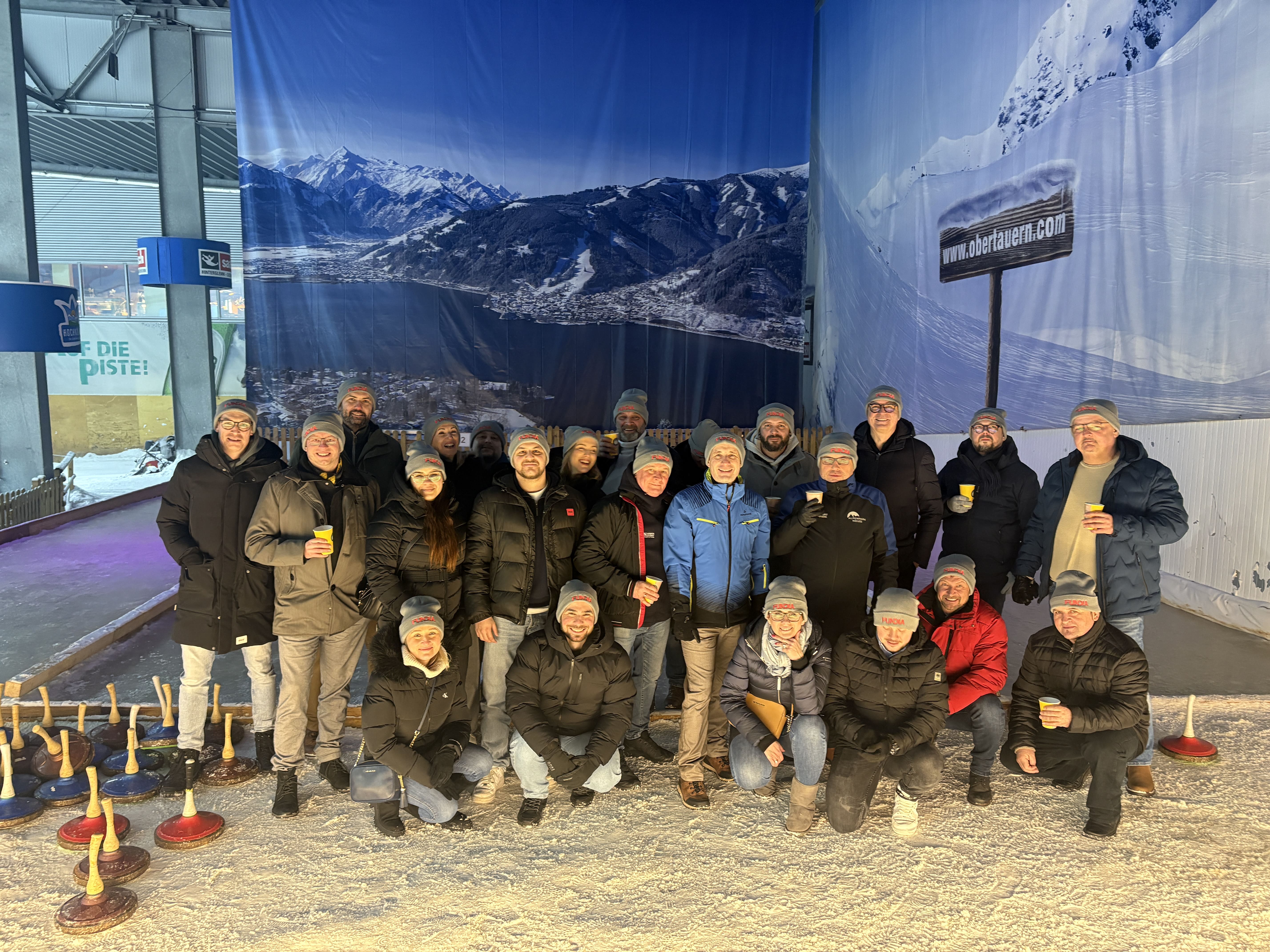 Das gesamte FUNDIA Team posiert geschlossen in Winterkleidung für ein Gruppenfoto auf der Eisstockanlage im Alpenpark Neuss.
